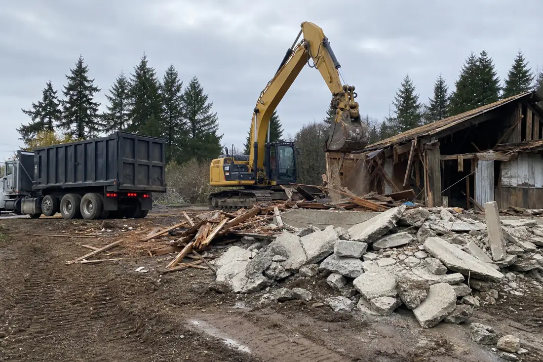 Excavator demolishing an old structure with a concrete and lumber debris pile in Hillsboro, OR