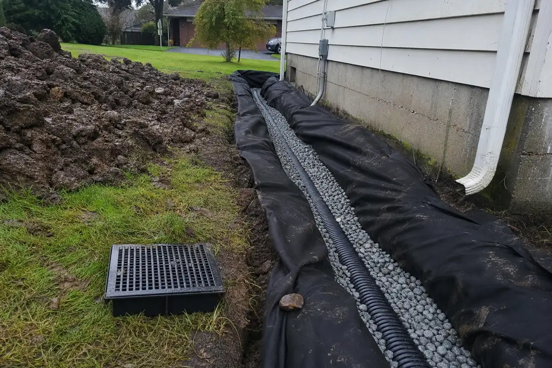 French drain trench with drain rock and perforated pipe along a house in Hillsboro, OR